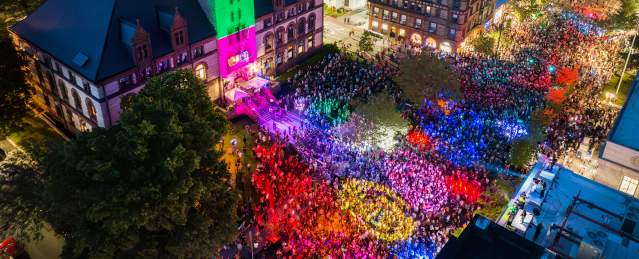 Aerial view at night of the Cambridge Dance Party, building and crowd illuminated by colorful lights
