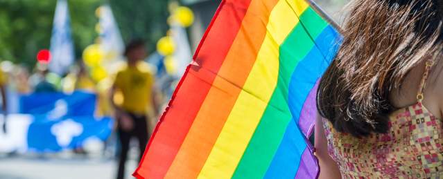 Back view of a person holding the rainbow flag over their shoulder