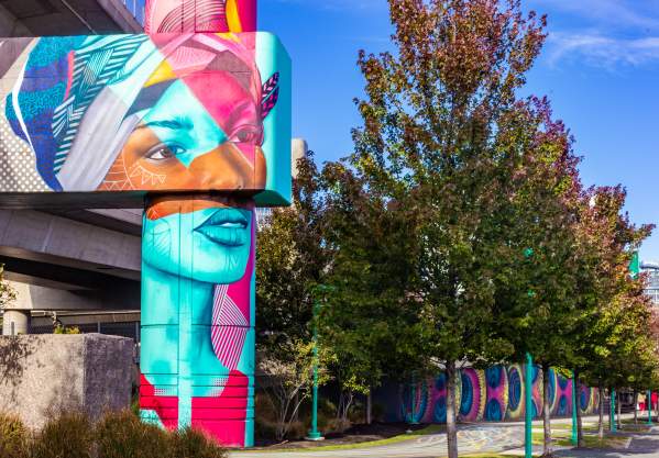 Woman's face with geometric shapes in turquoise, terracotta and magenta, painted on a cement column.