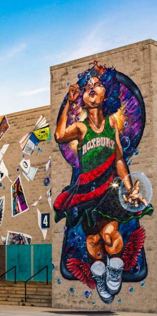 Mural depicting child wearing a dress reading Roxbury blowing bubbles and surrounded by blowing posters and books