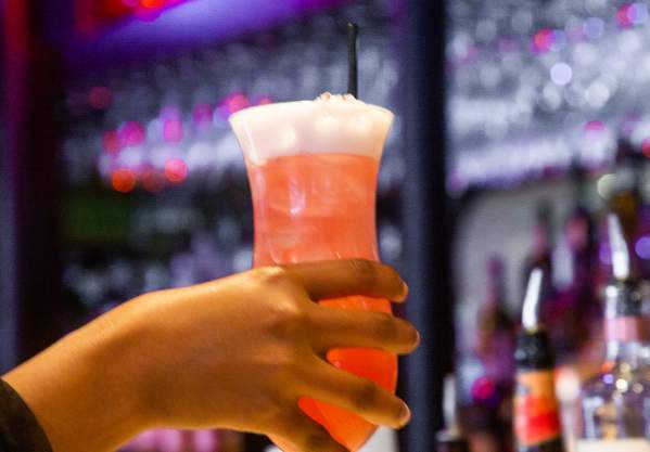 Hand holding a tall pink cocktail in front of the counter at Darryl's Corner Bar and Kitchen