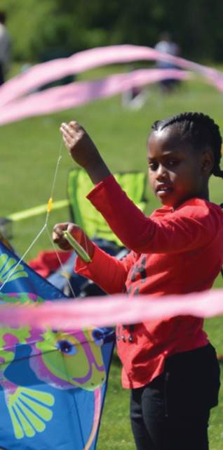 Child holding a kite at a Boston park with families in the background